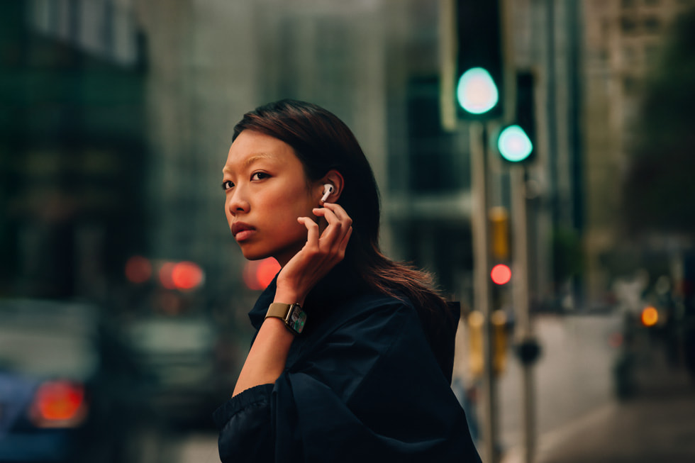 En person, der har AirPods 4 og Apple Watch Series 10 på, står på gaden i en storby. 