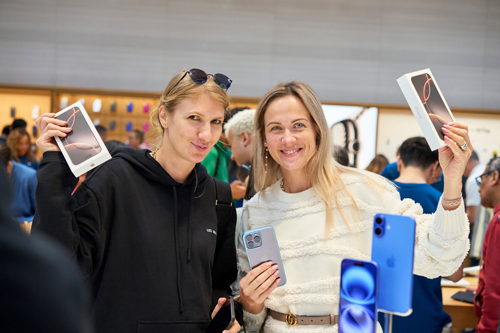 A smiling customer and a smiling team member hold up Phone 16 Pro boxes at Apple Fifth Avenue in New York City.