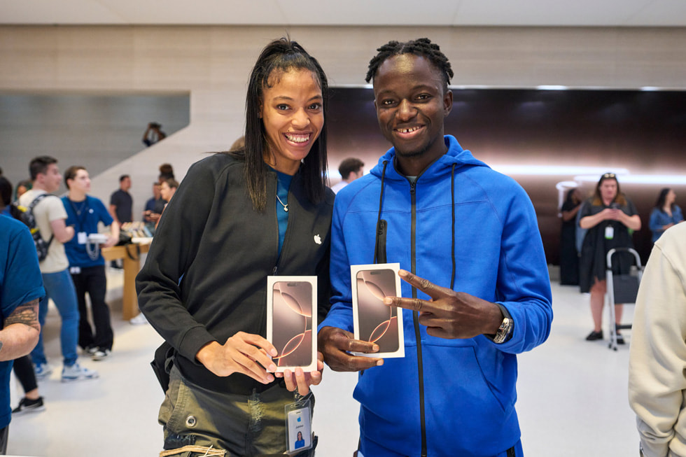 A smiling team member and a smiling customer hold up iPhone 16 Pro boxes at Apple Fifth Avenue in New York City.