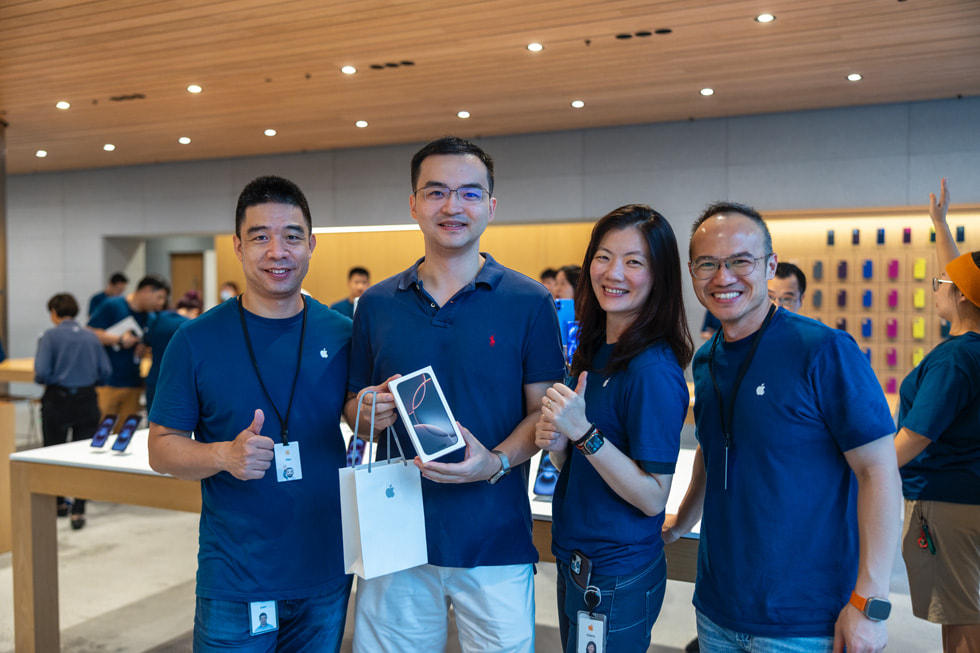 A customer shows off his new iPhone 16 Pro purchase as Apple team members cheer them on.