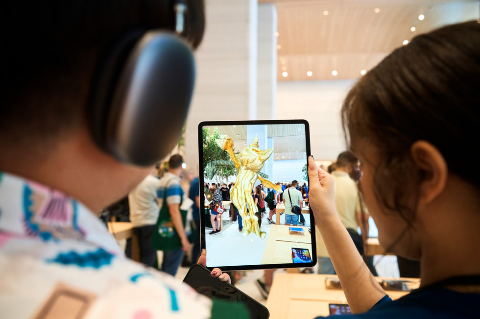 Członek personelu pokazuje klientowi, jak za pomocą iPada Pro obejrzeć w rzeczywistości rozszerzonej wystawę „United Visions” wewnątrz sklepu Apple Brompton Road.