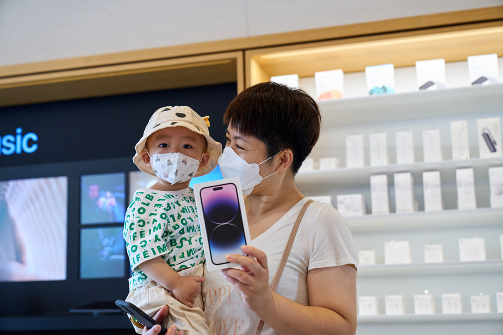 Cliente d’Apple Sanlitun avec un enfant dans les bras, montrant son nouvel iPhone 14 Pro.