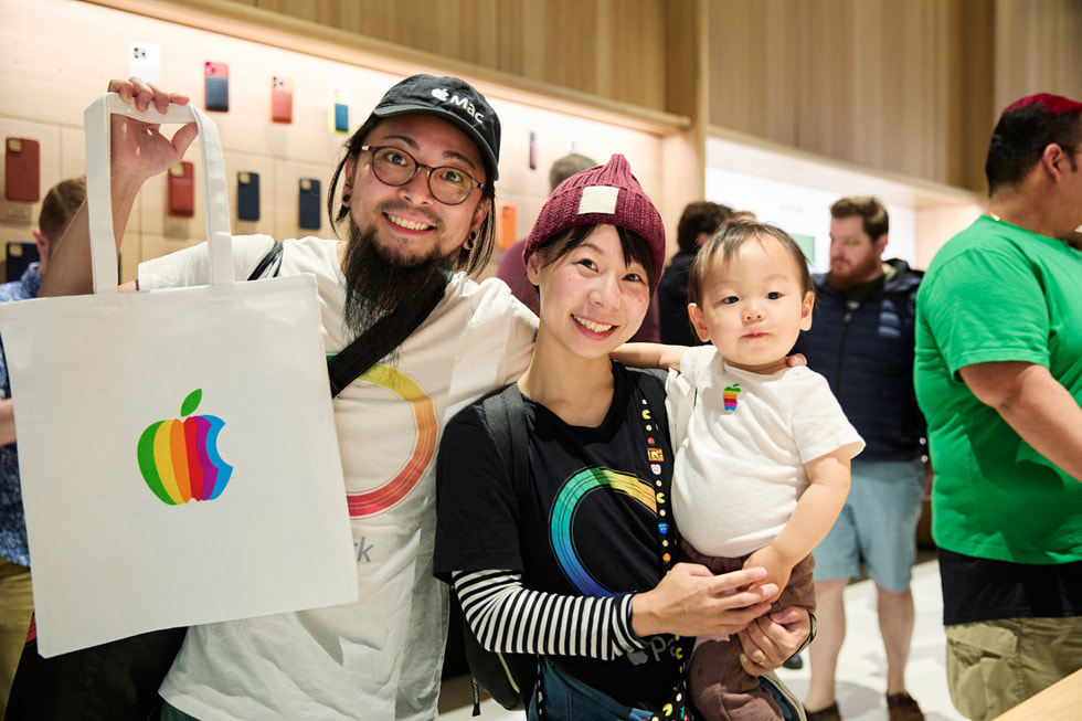 To kunder i klær med Apple-tema – den ene viser frem en Apple-bærepose og den andre holder en baby.