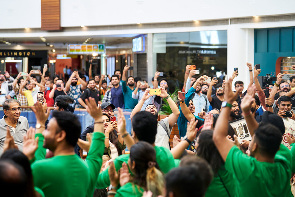 Een grote groep klanten in de rij voor Apple Saket. Veel klanten houden hun handen omhoog om foto’s te maken.
