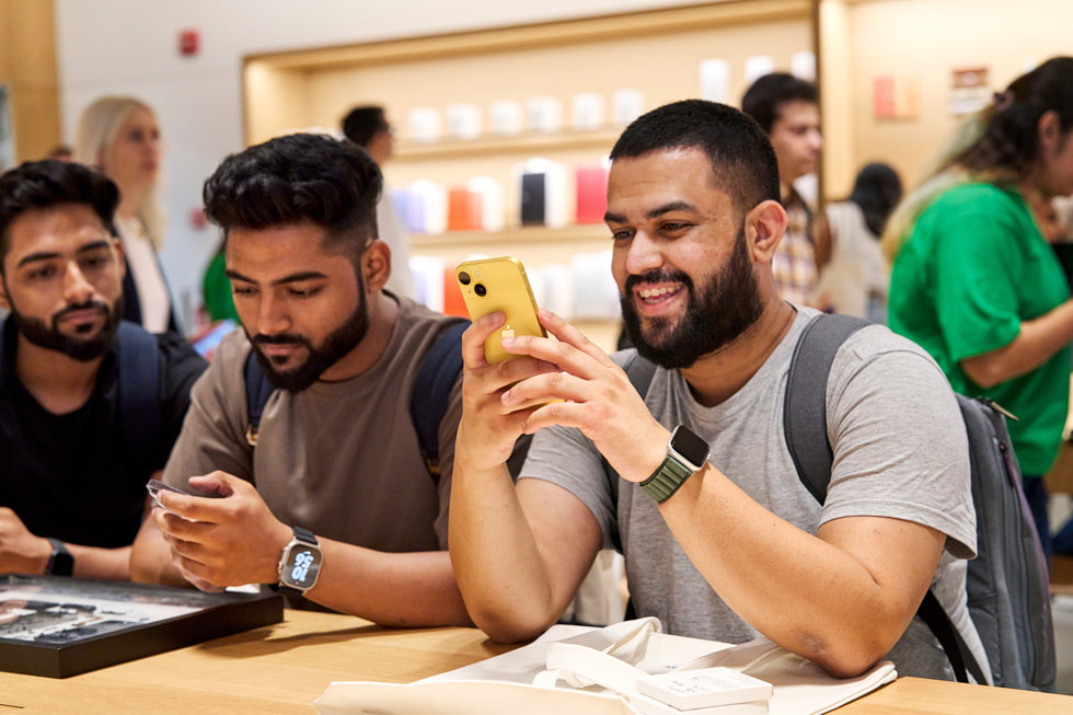 En kunde titter på nye iPhone 14 i gul ved et bord inne i Apple Saket.