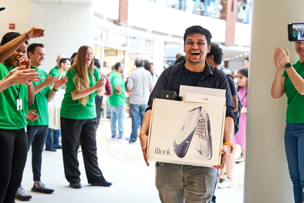 Medarbeiderne ser på når en smilende kunde viser frem en samling med eldre Apple-produkter.
