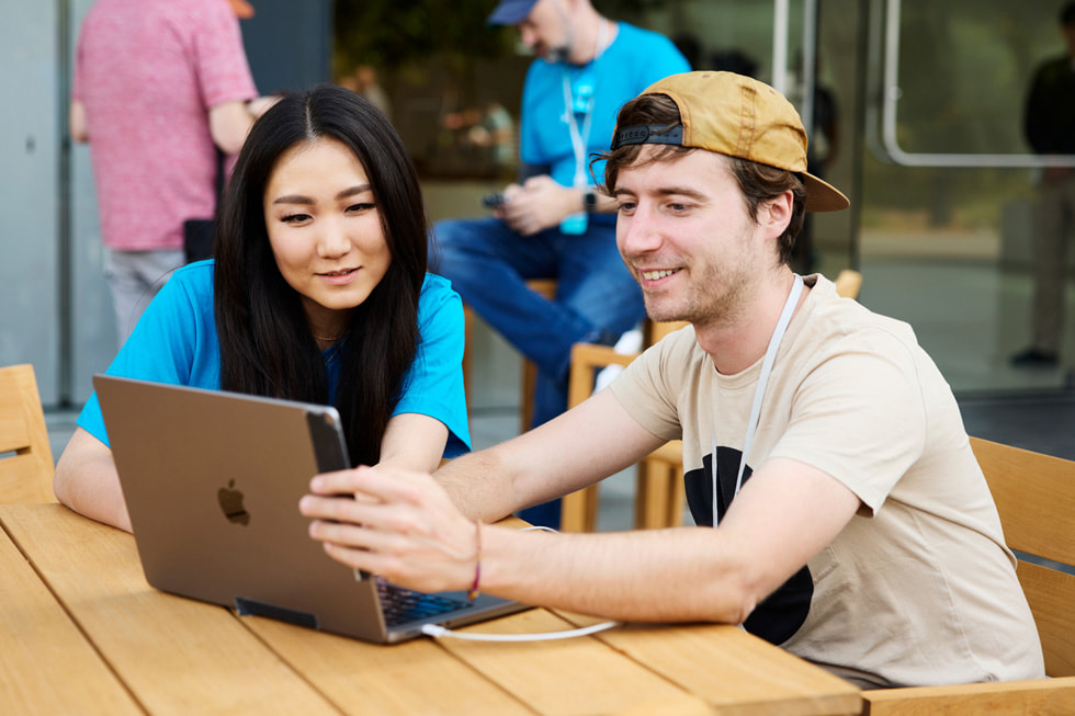 Zwei Personen beim Betrachten eines MacBook während des „Meet the Developers“ Events auf der WWDC23.