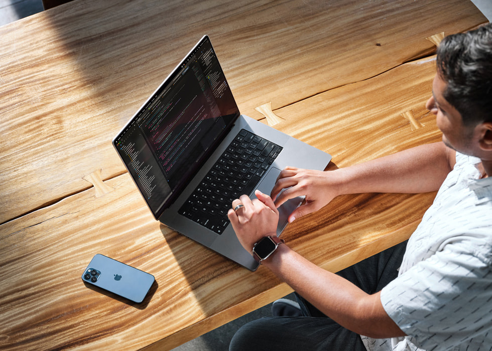Fågelperspektiv av Swupnil Sahai sittande vid ett skrivbord framför en MacBook Pro och med en iPhone vid sidan om.