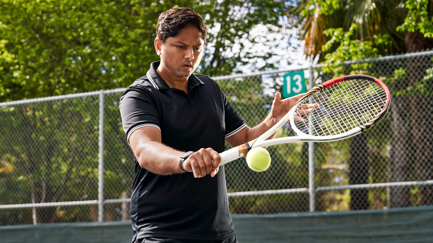 Sahai staat op de tennisbaan en speelt een tennisbal met de backhand.