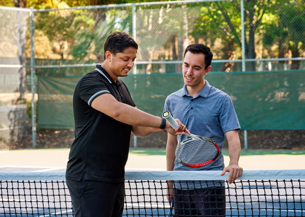 En la cancha, Sahai le muestra su Apple Watch a otro jugador de tenis.