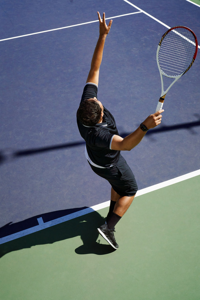 An overhead photo shows Swupnil Sahai, racket in hand, reaching up in the midst of a serve on a tennis court.