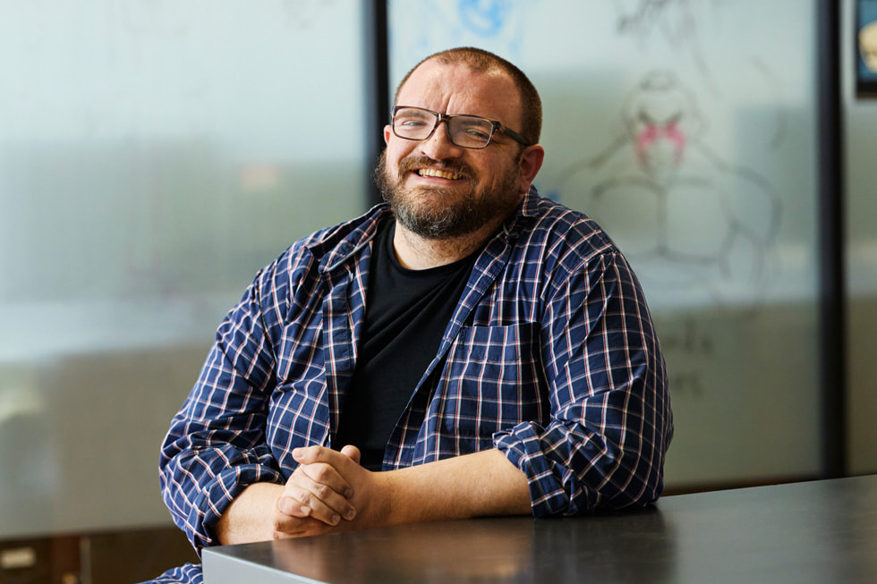 A portrait of academic dean Tim Dailey. Dailey is seated at a table and wearing a plaid button-down shirt over a black T-shirt, and a pair of glasses.