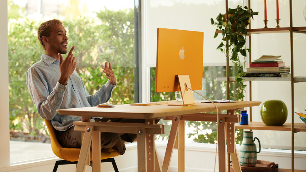 ホームオフィスに設定した新しいオレンジのiMacを使用している男性。