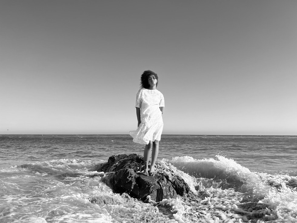 Okyanusun kıyısında ayakta duran bir kadının iPhone 13 Pro’nun Geniş kamerasında sensör bazlı OIS ile çekilmiş siyah-beyaz portresi.