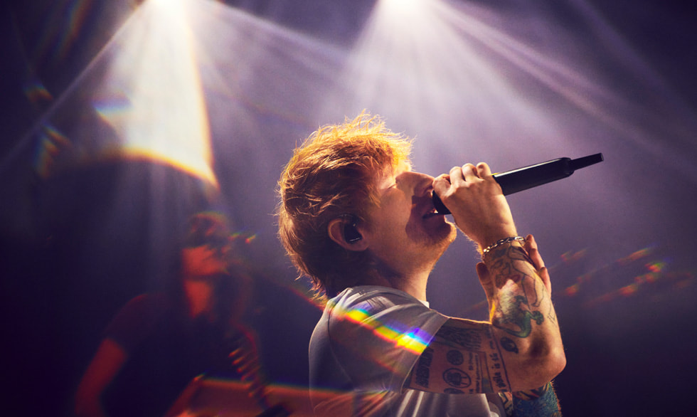 Singer-songwriter Ed Sheeran ses synge med en mikrofon på scenen.