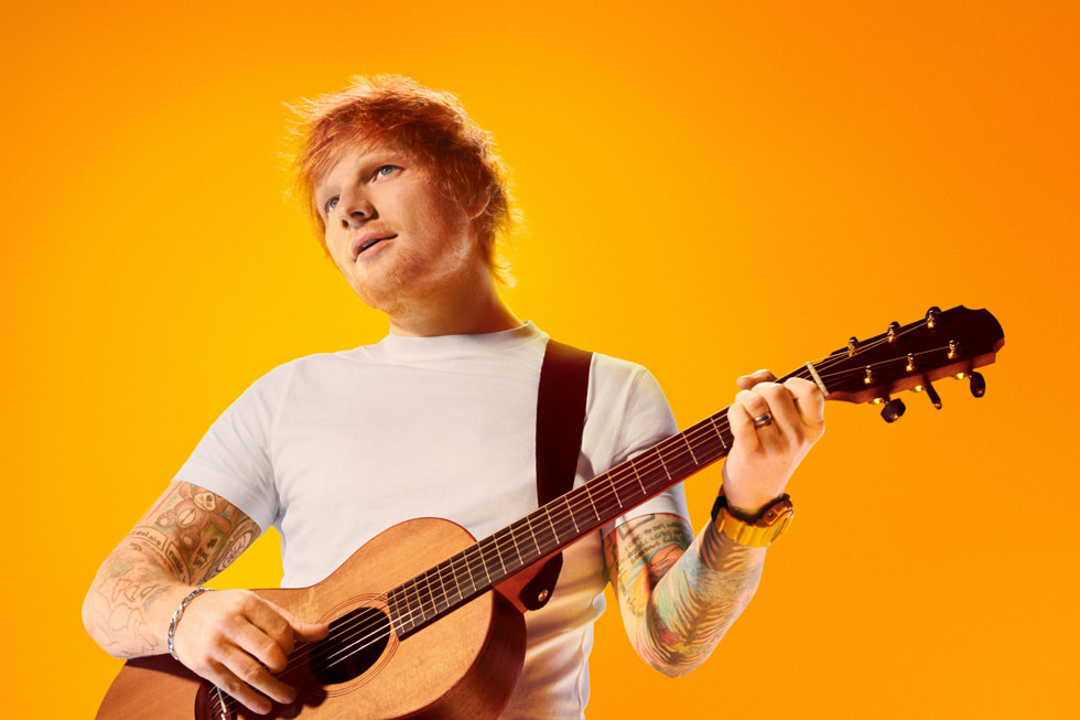 Sangeren og låtskriveren Ed Sheeran som spiller gitar, mot en oransje bakgrunn.
