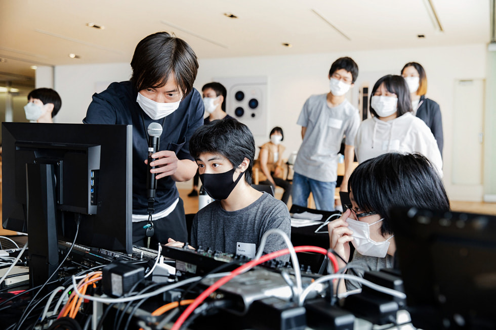 An Apple volunteer holding a microphone assists with the Creative Studios program in Tokyo with members of Sankakusha.