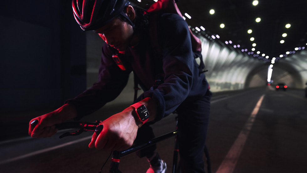 A cyclist wearing Apple Watch Series 7 rides through a tunnel at nighttime.