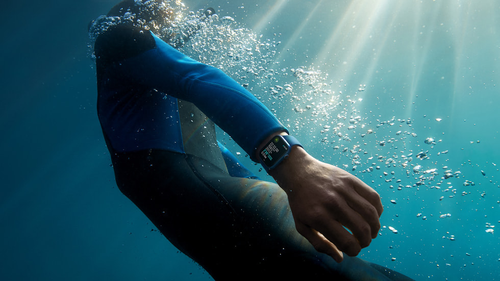 A surfer looks at Apple Watch Series 7 on their wrist in the ocean.
