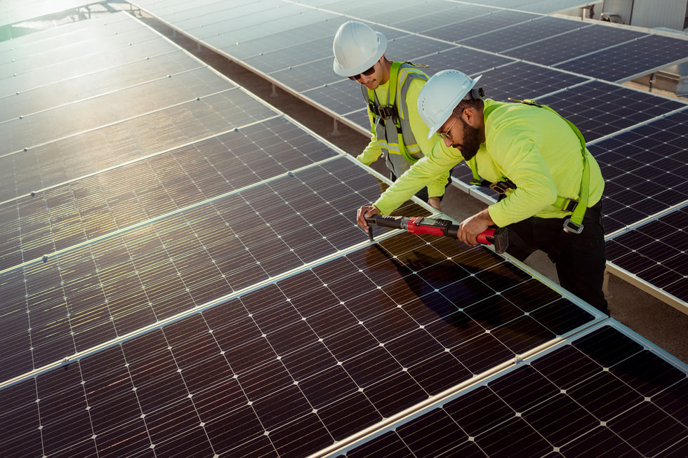 شخصان يرتديان خوذ واقية يعملون في منشأة للطاقة الشمسية في Bench-Tek Solutions في سانتا كلارا، كاليفورنيا.