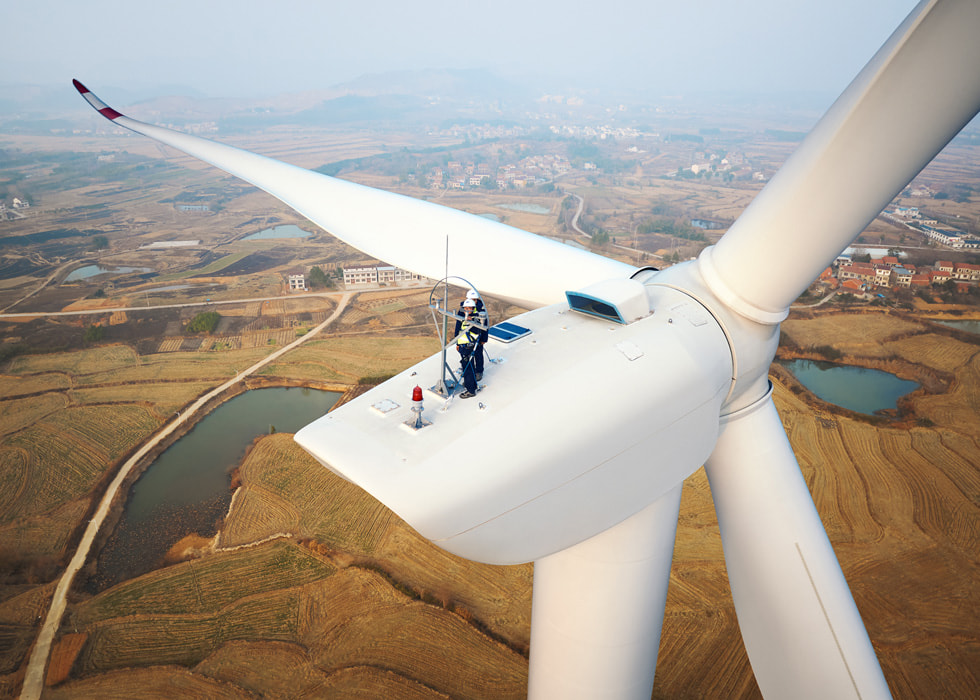 Zwei Arbeiter:innen auf einem in die Höhe ragenden Windrad in einem Windkraftprojekt in der chinesischen Provinz Hubei.