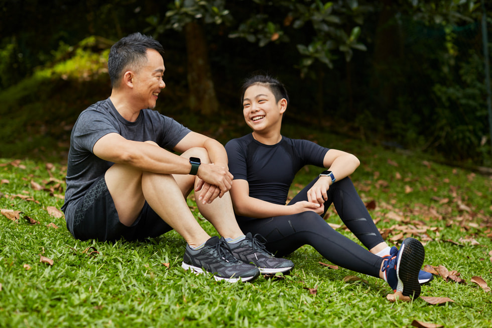 LumiHealth user Benjamin Lee and his son in their workout attire sitting on a grassy hill, both wearing Apple Watch.