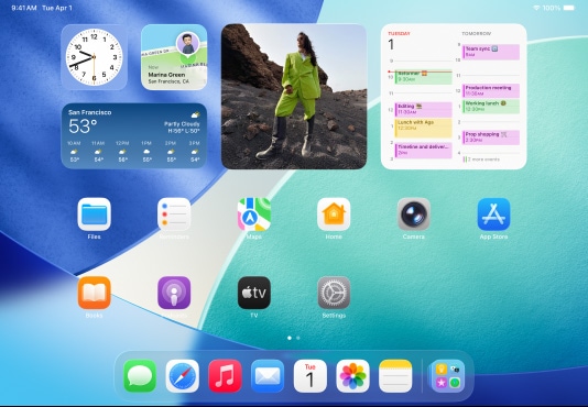 iPad, trzy modele, w orientacji poziomej, model środkowy przed dwoma pozostałymi, Apple Pencil przymocowany magnetycznie do górnej części środkowego modelu, na którego ekranie widać ekran początkowy, przedstawiający kolorowe ikony aplikacji z efektem Liquid Glass, lewy ekran przedstawia apkę Podgląd, na prawym widać ekran początkowy i rozchodzące się półkoliście z Docku pliki