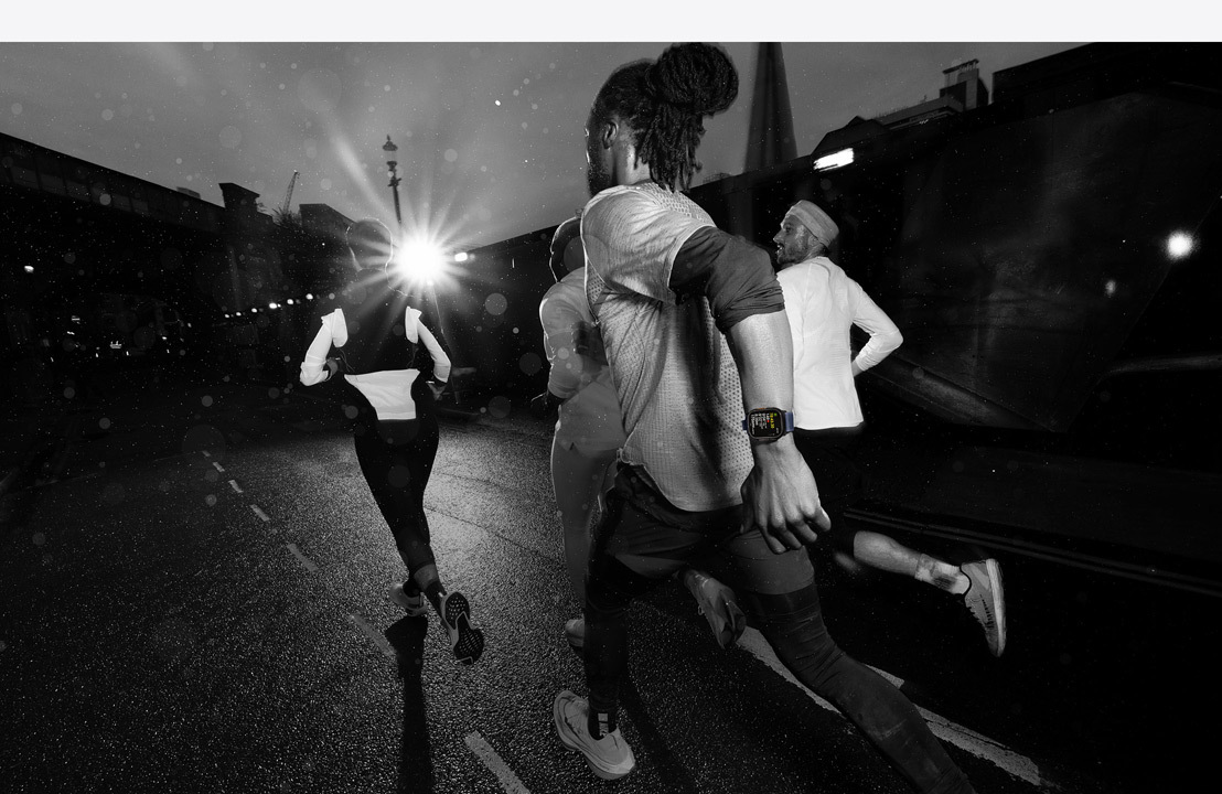  Four people wearing Apple Watches running through the city after dark.