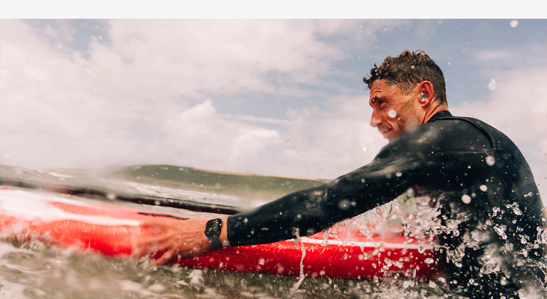  A man in a wetsuit wearing an Apple Watch Series 10 preparing to paddle out in the surf.