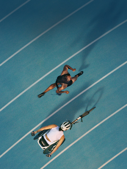 Two athletes racing each other on a track, one is running and the other is ina racing wheelchair.