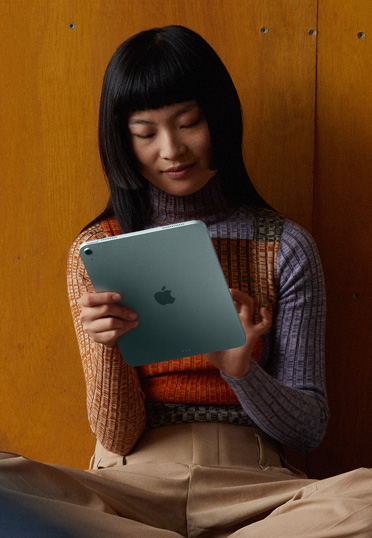 นักศึกษานั่งพิงผนัง และถือ iPad อยู่ในมือ