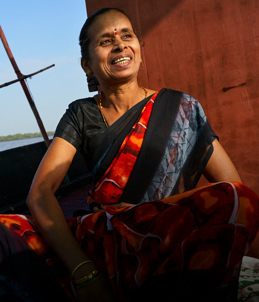 Una mujer india sonríe sentada en un barco, con una vía fluvial al fondo