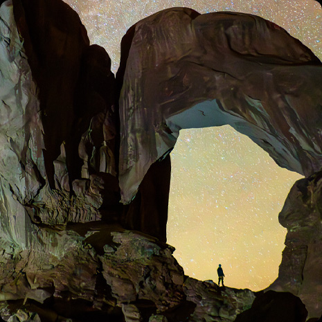 Photograph of a person in a canyon and a star-filled night