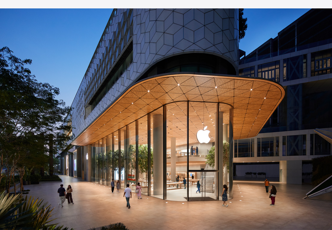 Apple 直營店夜景圖,展示玻璃窗戶、來自室內的燈光,以及正門上方中央的 Apple 標誌。