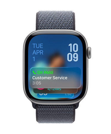 Uhlově černé Apple Watch se šalvějově šedým řemínkem, ve spodní části ciferníku se zobrazuje oznámení funkce Asistované podržení, vlevo nahoře datum, vpravo nahoře čas psaný číslicemi nad sebou